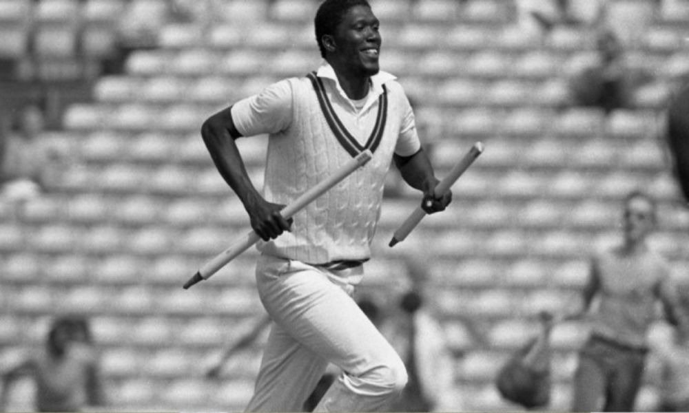 Joel Garner is celebrating a wicket while holding two stumps during a match.