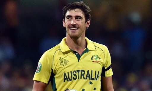 Australian cricketer in a yellow team jersey smiling while holding a cricket ball on the field during a match.