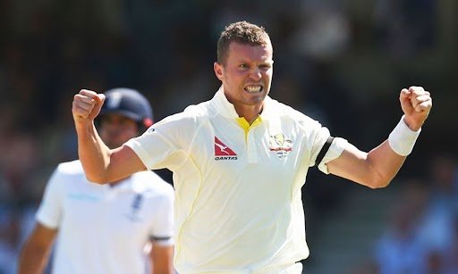 Australian cricketer in a white uniform celebrating with clenched fists after taking a wicket during a match, with another player in the background.