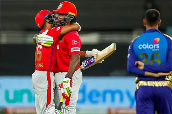 Punjab Kings batsmen hugging after a partnership while a Mumbai Indians fielder watches in the background