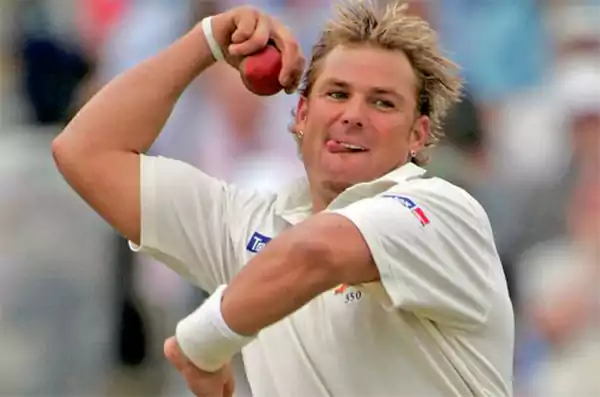 Shane Warne bowling in a white cricket uniform taking 1001 international wickets